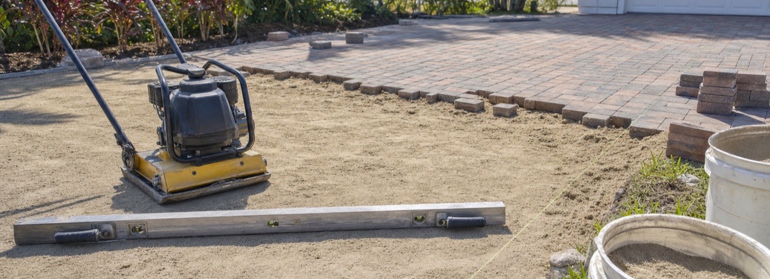 Plate compactor and screed level on prepared bedding sand during paver re-leveling